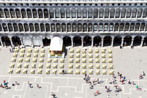 Venezia, Italy - 1st July 2013: Cafe-bar patio with empty tables and chairs & some tourists moving chaotically in San Marco Square, mid day. Shot from Museo Correr balcony.