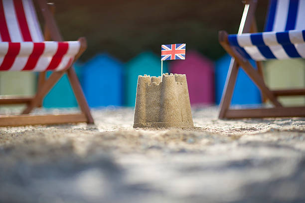 Sandcastle with UK flag between two deck chairs sandcastle between two deckchairs with a uk flag in it  beach hut stock pictures, royalty-free photos & images