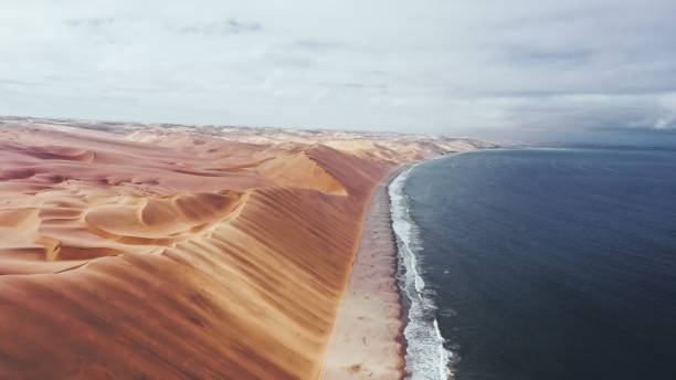 Sandwich Harbour Namib Naukluft National Park Namibia large mighty sand dunes stretch out over the ice-cold atlantic sea Namib Desert stock pictures, royalty-free photos & images
