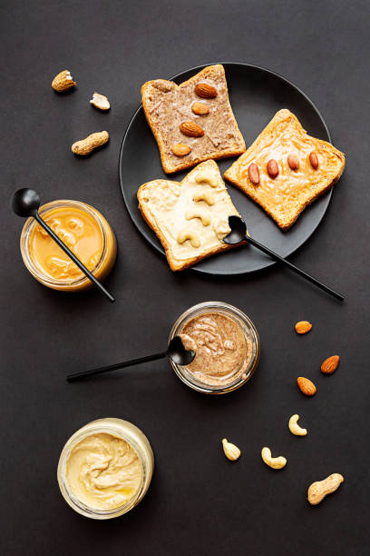 Sandwiches with peanut, cashew and almond butter, jars of nut butters on a black background. The modern concept of healthy eating and veganism. Sandwiches with peanut, cashew and almond butter, jars of nut butters on a black background. The modern concept of healthy eating and veganism. almond butter stock pictures, royalty-free photos & images
