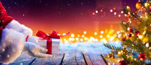 weihnachtsmann verschenkt geschenke unter dem weihnachtsbaum mit abstrakten lichtern in der nacht - romolotavani stock-fotos und bilder