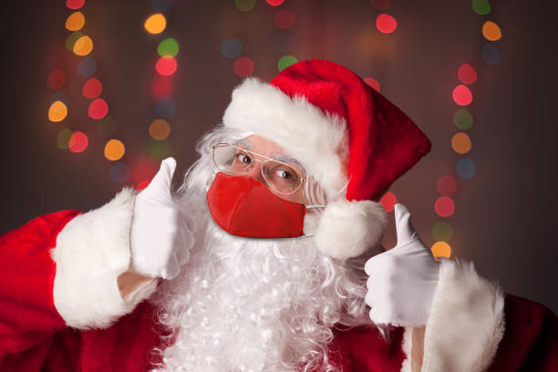 weihnachtsmann in gesichtsmaske mit zwei daumen nach oben - santa stock-fotos und bilder