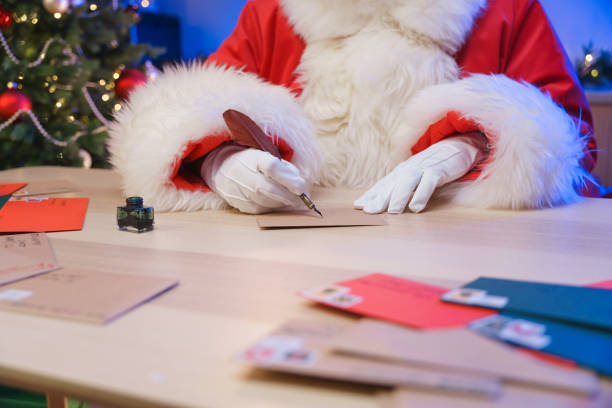 Santa Claus is writing a letter next to a Christmas tree stock photo