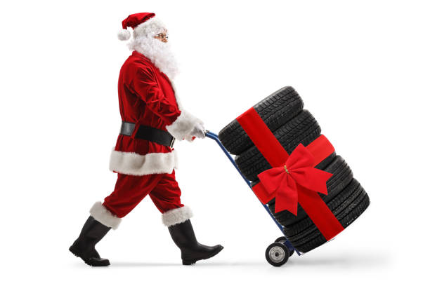 Santa claus pushing car tires tied with a red bow on a hand truck stock photo