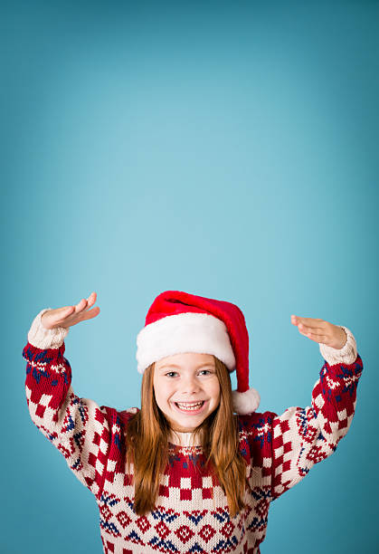 Santa's Happy Little Helper Wearing Hat and Christmas Sweater Color image of a happy little girl wearing a Santa hat and an ugly Christmas sweater. Includes copy space. ugly girl stock pictures, royalty-free photos & images