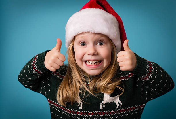Santa's Little Helper Giving Thumbs Up Sign Color image of a little girl giving "thumb's up" sign. She is wearing a Santa hat and an ugly Christmas sweater. ugly girl stock pictures, royalty-free photos & images