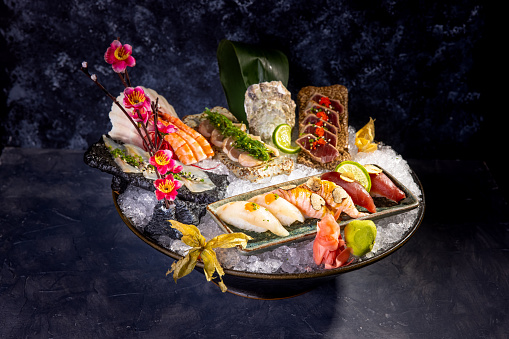 Raw food in decorated serving dish full of ice, nigiri, tataki, prawn and tuna slices with ginger and wasabi