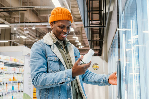 Satisfied African man in a supermarket selects bottled milk from the refrigerator and reads the composition of the product stock photo