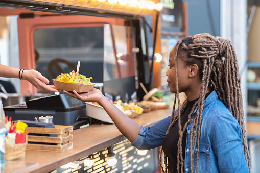 Afro american woman getting a delicious looking tray with nachos from a fast food truck. Selective focus: Fast food and lifestyle concept.