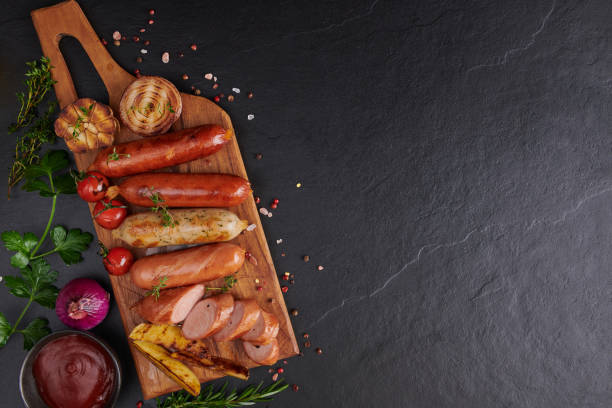 sausages and ingredients for cooking. Grilled sausage with the addition of herbs and and spices, vegetables, rosemary, thyme on the grill plate, Grilling food, bbq, barbecue, on stone table. Top view. stock photo