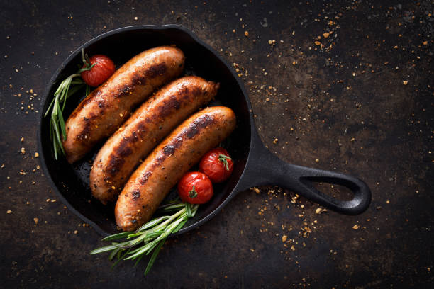 Sausages in a skillet Three sausages in a cast iron skillet with seasoning sausage stock pictures, royalty-free photos & images