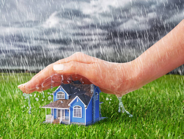 Save house. Hand protecting house from rain on a overcast weather background. stock photo