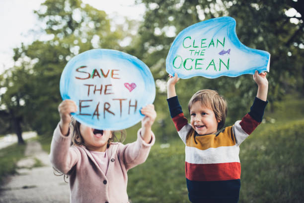 Save our childhood by saving the environment! Happy kids holding placards for environmental conservation at the park. Focus is on boy. rescue stock pictures, royalty-free photos & images