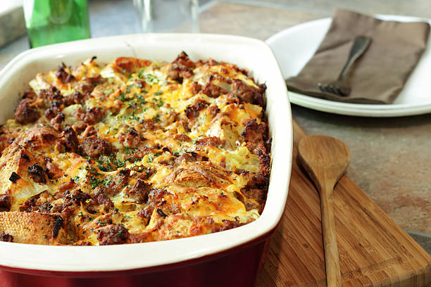 Savory breakfast casserole next to wooden spoon A bread pudding casserole made from French baguette bread, sage breakfast sausage, onions and cheddar cheese casserole stock pictures, royalty-free photos & images