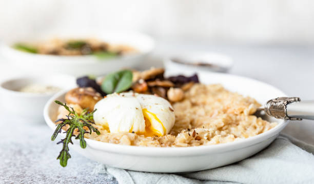 Savory porridge for breakfast. Oatmeal or spelt flakes with poached egg, fried mushrooms and herbs. Healthy food. Keto diet. Cose up. stock photo