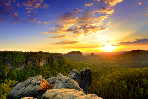 Saxon switzerland elbsandstone yellow sunrise at national park rock peak above green forest blue sky morning clouds