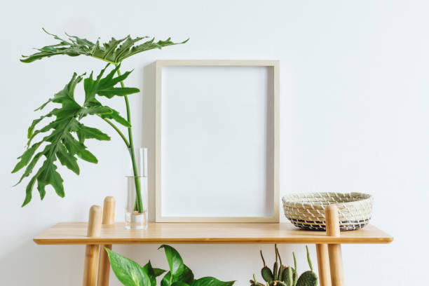 Scandinavian room interior with mock up photo frame on the brown bamboo shelf with beautiful plants, tropical leafs and accessories. White walls. Modern and floral concept of shelfs. Minimalistic home interior with composition of home garden. Plants love. scandinavian culture photos stock pictures, royalty-free photos & images