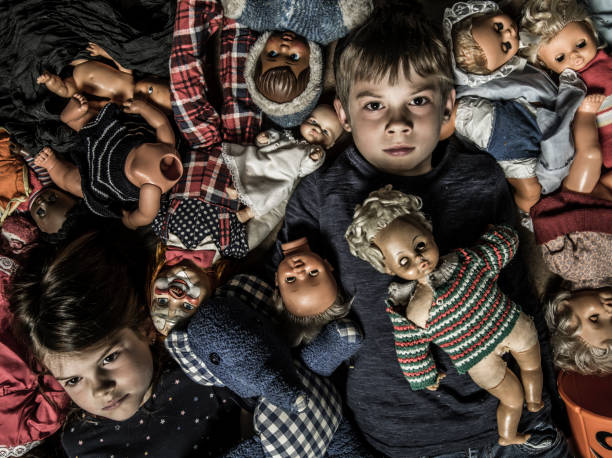 Scary children in a pile of creepy dolls Photo of creepy young children on the floor surrounded by old dolls for Halloween theme. broken doll 1 stock pictures, royalty-free photos & images