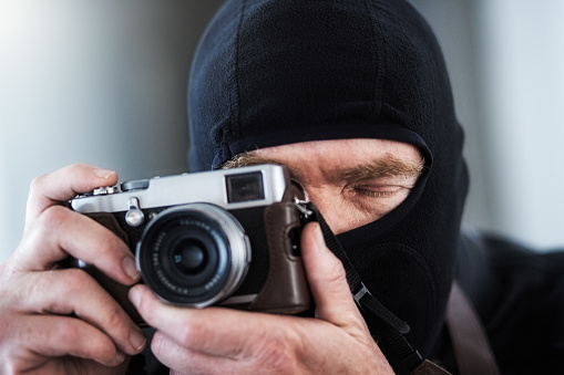 Ominous mature man wearing ski mask and concentrating as he takes a photograph with a retro camera.