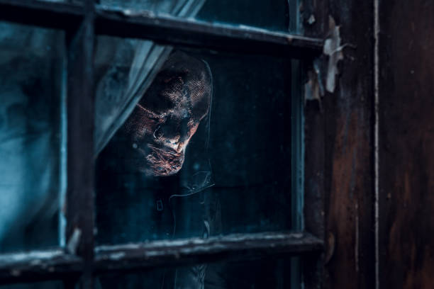 Scary man wearing a horror mask looking through the window from inside the house. stock photo