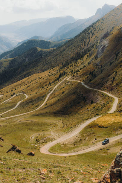 Scenic aerial view of car driving the curved mountain pass at Tian Shan mountains, Kyrgyzstan Picturesque mountain road with view of the colorful peaks in Central Asia and black car driving down through it silk road stock pictures, royalty-free photos & images