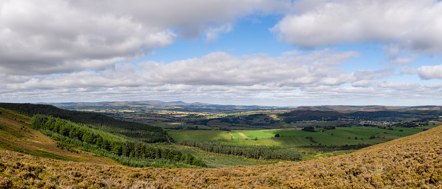 A panoramic of the rolling landscape in Rothbury, Northumberland taken from a viewpoint. The sun is shining and the clouds are moving over the land.