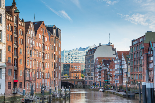scenic view of historic buildings on both sides of Nikolaifleet channel in Hamburg, Germany with Elbphilharmonie concert hall in background under beautiful summer sky