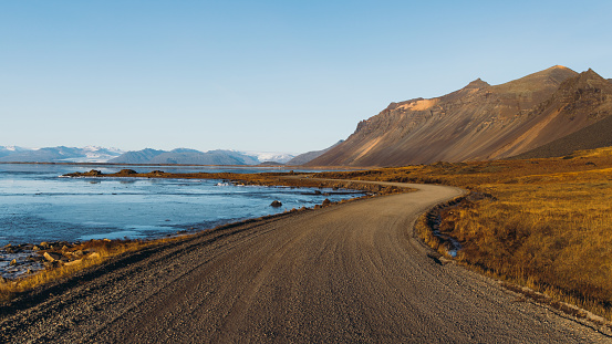 Panoramic photo of thew gravel road with view of the beautiful mountains and the frozen sea in West Iceland