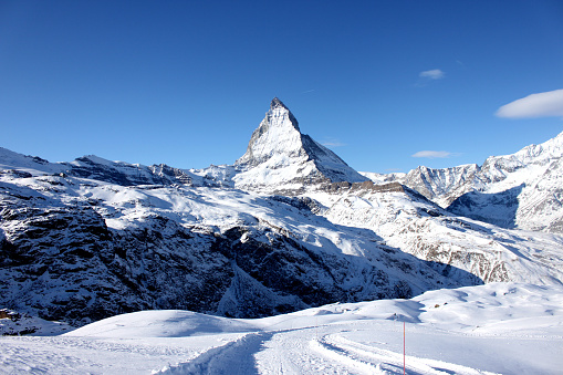 Scenic view on snowy Matterhorn peak in sunny day with blue sky and some clouds in background.