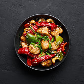 Schezwan Chicken or Dragon Chicken in black bowl at dark slate background. Szechuan Chicken is popular indo-chinese spicy dish with chilli peppers, chicken and vegetables.