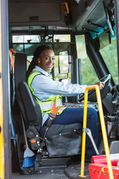 School bus driver looking through doorway A mature African-American woman in her 40s driving a school bus. She is sitting in the driver's seat wearing a reflective vest, looking toward the camera, through the open door. school bus driver stock pictures, royalty-free photos & images