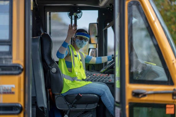 School bus driver wearing protective wear during COVID-19 Female bus driver wearing a protective face mask and shield while driving a school bus during COVID-19 to avoid the transfer of germs. school bus driver stock pictures, royalty-free photos & images