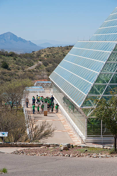 School Children Tour Biosphere 2 "Oracle, United States - March 23, 2012: A group of school children tour Biosphere 2, an extensive science research facility originally created to study the interaction between Earth's life systems in a closed environment.  Two separate missions were initially launched with scientists sealed within the vivarium for up to two years.  They studied five different biomes: rainforest, ocean with a coral reef, mangrove wetlands, savannah, and desert.  The complex is now run by the University of Arizona and is considered a place where research, teaching and studying the Earth's living systems can be accomplished in the world's largest closed system ever created." biosphere 2 stock pictures, royalty-free photos & images