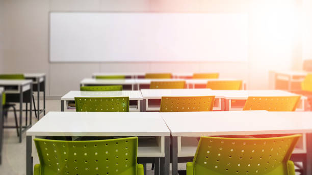 School classroom in blur background without young student; Blurry view of elementary class room no kid or teacher with chairs and tables in campus.  lecture hall stock pictures, royalty-free photos & images