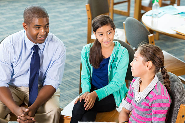 School counselor meeting with elementary students Mid adult African American man is teacher or school counselor. He is meeting with elementary age Hispanic little girls after school to discuss issues or bullying. Teacher is listening while girls talk about problems. school counselor stock pictures, royalty-free photos & images