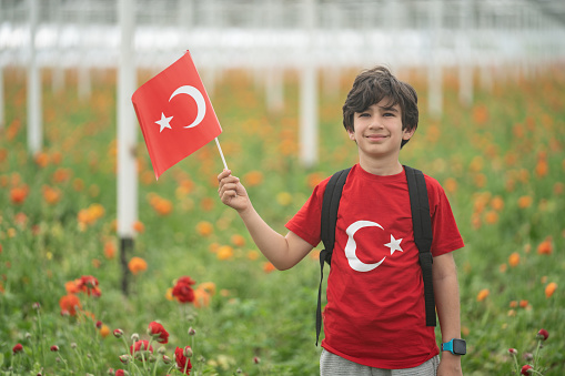 Photo of elementary school boy with Turkish flag in flower garden celebrating April 23 National Sovereignty and Children's Day, that is Ulusal Egemenlik ve Çocuk Bayramı.. Shot under daylight.