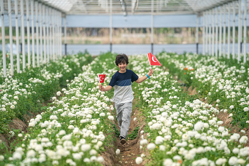 Photo of elementary school boy with Turkish flag in flower garden celebrating April 23 National Sovereignty and Children's Day, that is Ulusal Egemenlik ve Çocuk Bayramı.. Shot under daylight.