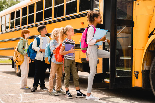 Schoolchildren kids pupils group of mixed-race classmates boarding school bus before going to lessons, coming back to school, standing in line. New educational year semester. stock photo