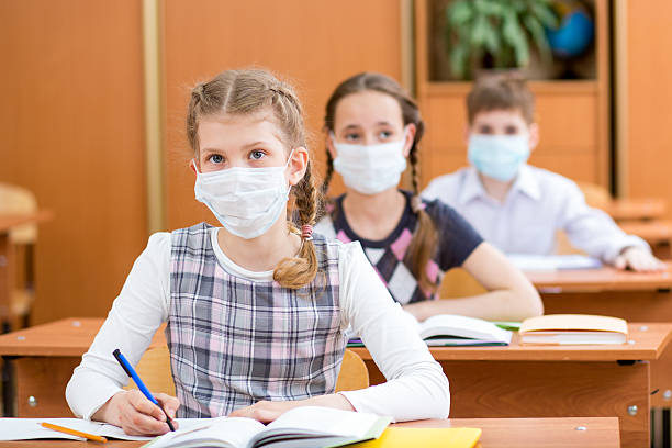 schoolkids with protection mask against flu virus at lesson stock photo