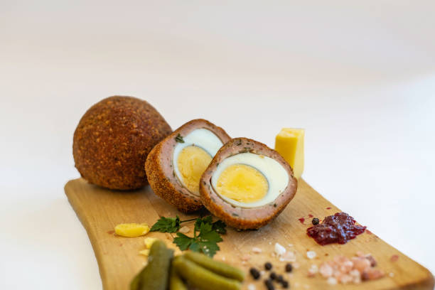 Scotch Eggs on wooden platter with traditional English Cheddar Cheese, Gherkins, condiments and garnish. stock photo