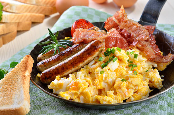 Scrambled eggs and sausages Scrambled eggs with fried bacon and sausages served in a pan with toast bacon stock pictures, royalty-free photos & images