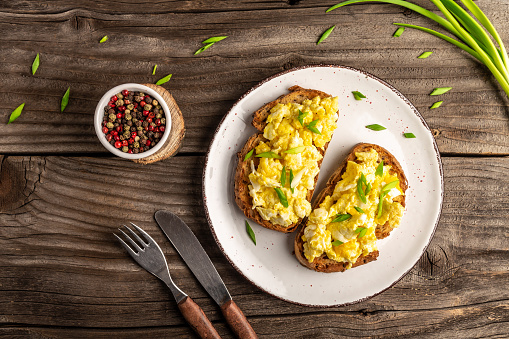 Scrambled eggs with green onion on wheat rye wholemeal crispy bread, homemade, healthy breakfast or brunch. Homemade meal, banner, menu recipe place for text, top view.