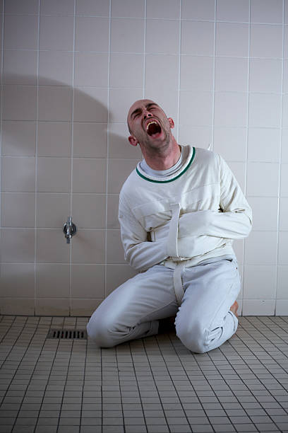 screaming-psychopath-into-a-straightjacket-sits-on-a-tiled-floor-picture-id133998440