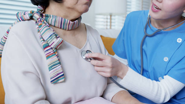 Scrub nurse doctor using stethoscope exam check heartbeat old asia female at home in elderly care cardiovascular medical visit, cardiology cholesterol problem and hospice healthcare caregiver concept. stock photo