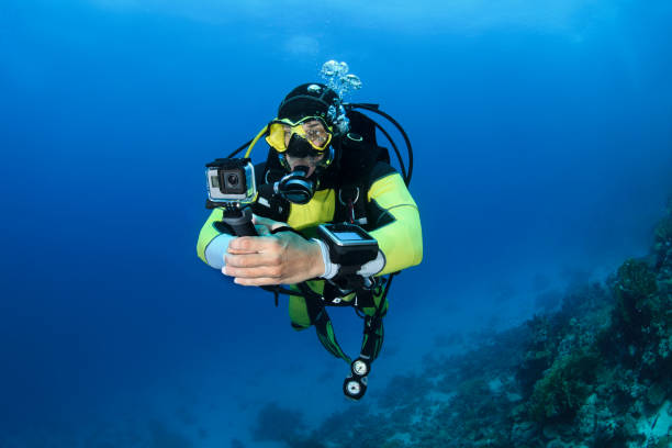 Scuba diver using a GoPro while diving underwater Male scuba diver using an action camera to take some underwater shots. aqualung diving equipment photos stock pictures, royalty-free photos & images