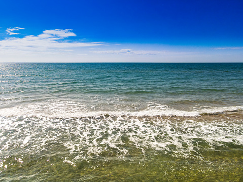 Sea, blue sky and horizon - photo of foaming ocean waves and blue sky with clouds. Blue open sea. Horizon over water. The horizon line. Sea waves against the sky. Blue sky with clouds. White clouds and white waves. Clear water and blue sky. Ocean shore, waves and shore. Seascape.
