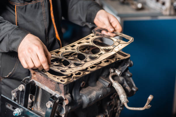 Sealing gasket in hand. The mechanic disassemble block engine vehicle. Engine on a repair stand with piston and connecting rod of automotive technology. Interior of a car repair shop. stock photo