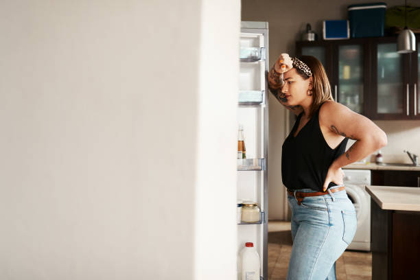 Searching for the answer to life's great questions Shot of a young woman searching inside a refrigerator at home hungry stock pictures, royalty-free photos & images