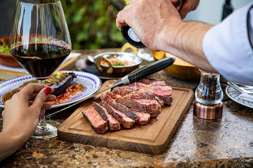 Seasoning juicy medium rare beef steak with salt grinder, cut on wooden board on restaurant table