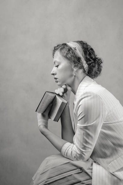 Seated young woman, dressed in retro style, holding a book stock photo